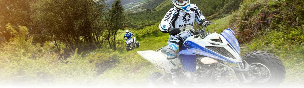 Two individuals riding Yamaha® ATVs up a wooded hill.